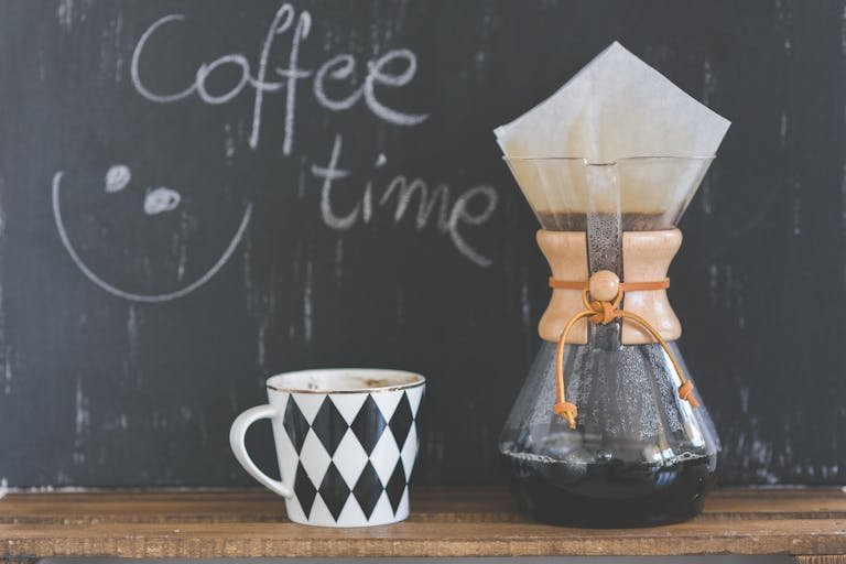 A cozy café scene featuring a Chemex with freshly brewed coffee and a patterned mug, perfect for morning rituals.